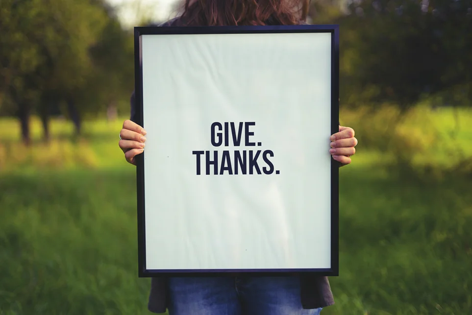 Person holding a sign in nature with the words 'GIVE THANKS' to promote gratitude exercises for daily positivity